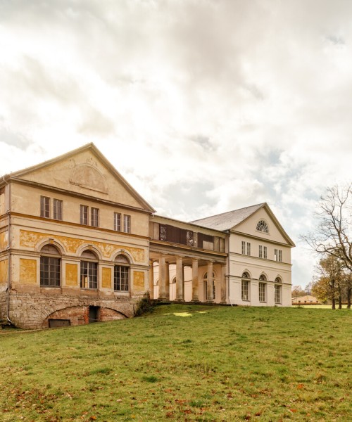 Schloss Wilhelmsthal bei Eisenach mit klassizistischer Fassade und Parklandschaft, herbstliche Bäume und weitläufige Wiese unter hellem Himmel.