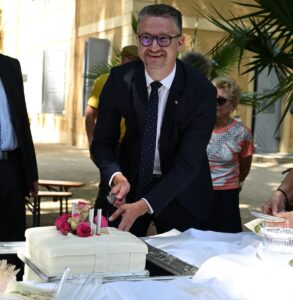 Ehrengast Minister Tischner schneidet weiße Jubiläumstorte mit rosa Blüten bei der Eröffnung „50 Jahre SATIRICUM“ im Sommerpalais Greiz an.