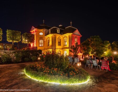 Illuminiertes Rokokoschloss Dornburg bei Nacht, mit festlich beleuchtetem Garten, Besucherinnen und Besuchern auf Stühlen unter Bäumen – Aufnahme während der Dornburger Schlössernacht im Sommer in Thüringen.